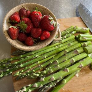 A bowl of strawberries and fresh asparagus on a table.