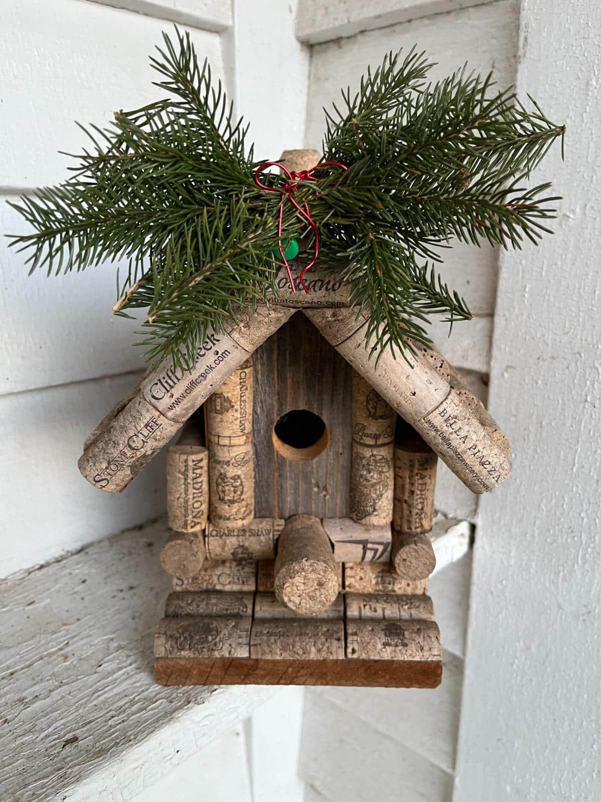 A bird house accented with Christmas tree trimmings